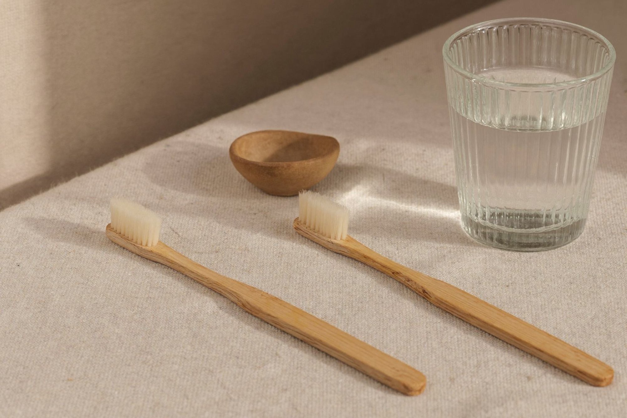 Two bamboo toothbrushes beside a glass of water