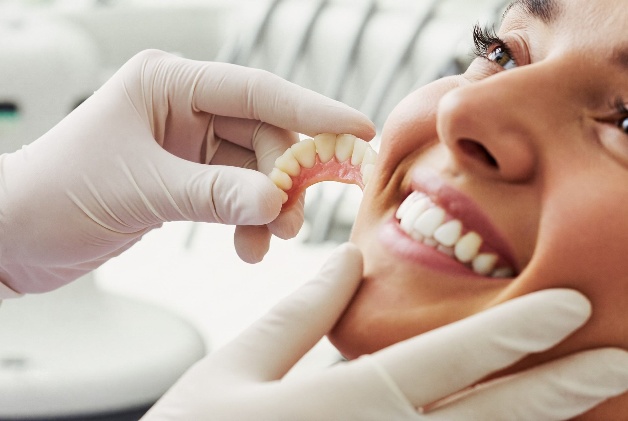 Dentist in white gloves fitting a dental restoration to a smiling patient's teeth
