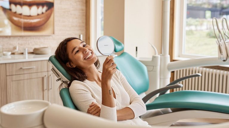 Smiling woman checking her teeth in a hand mirror in the dental chair