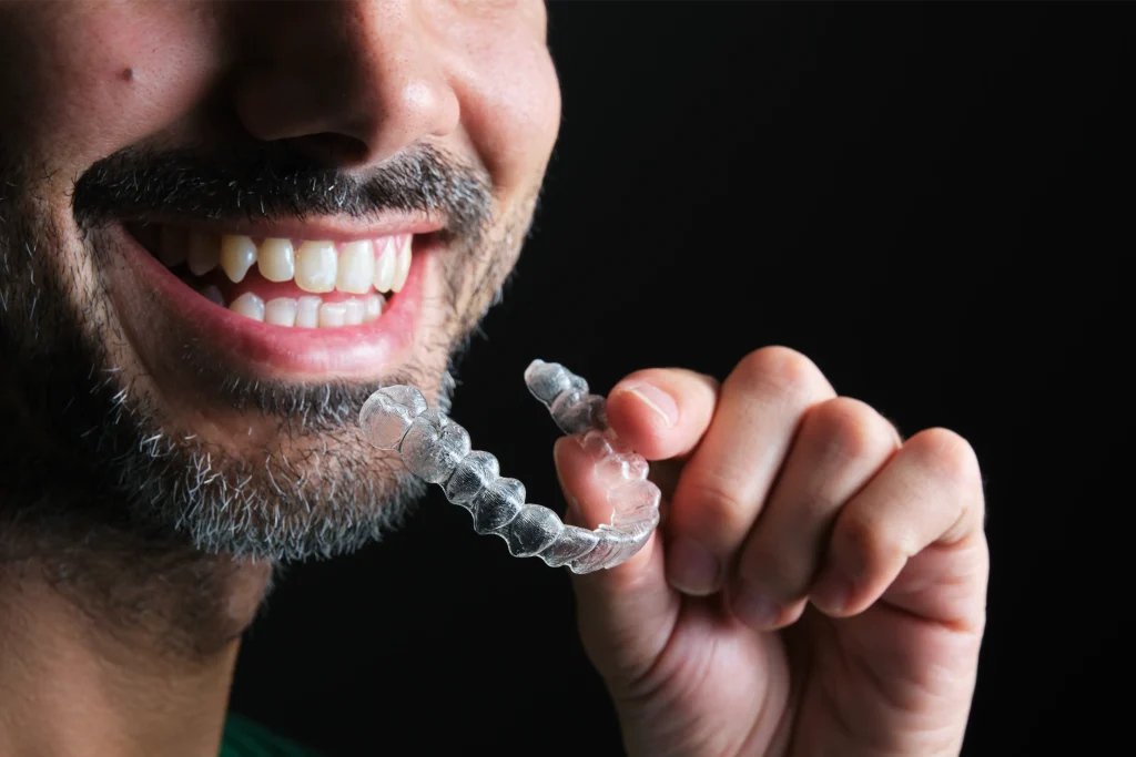 Smiling man holding a clear dental aligner