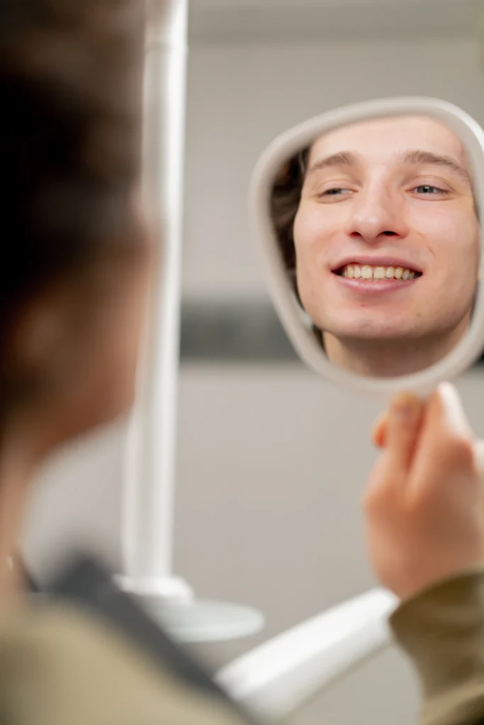 Patient checking his smile in a hand mirror at the dentist